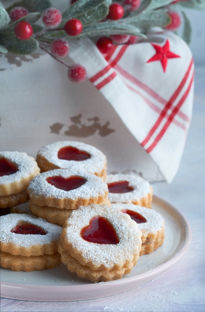 Plate of traditional Christmas Linzer cookies filled with strawberry jam on white table with Xmas decorations