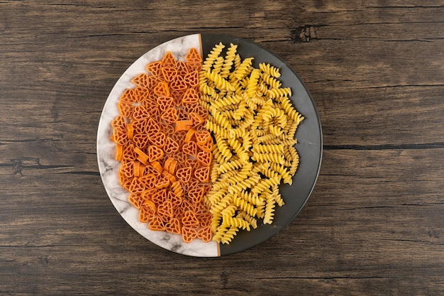 Plate of two various uncooked pasta on wooden table.