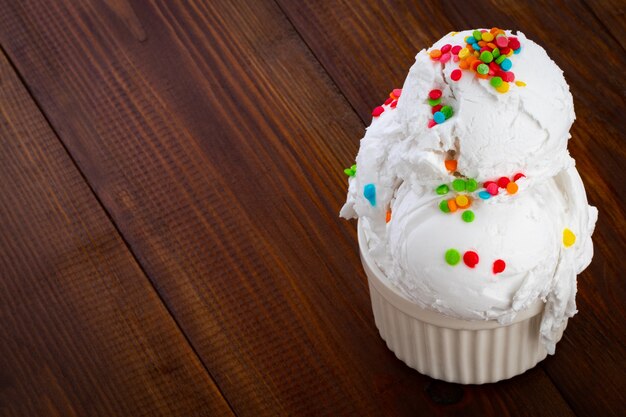 Plate of vanilla ice cream scoop swith sprinkles on wooden background with copy space.