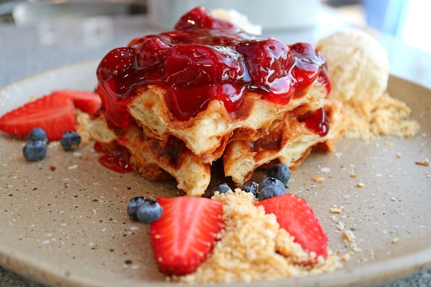 Plate of waffle with strawberry sauce, fresh berries and vanilla ice cream