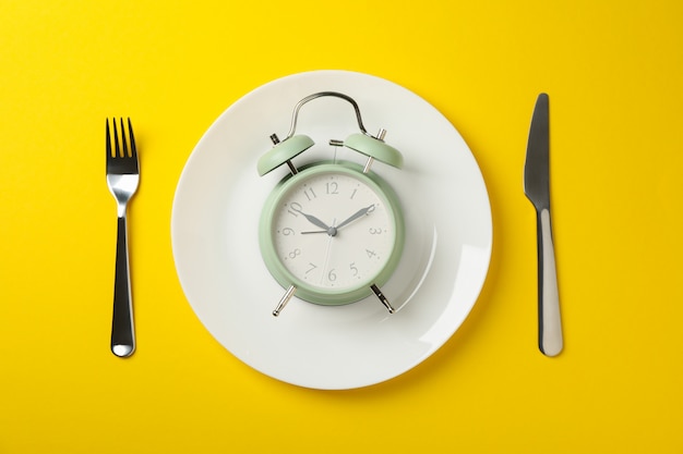 Plate with alarm clock, fork and knife on yellow