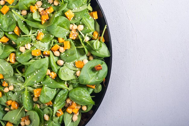 Foto piatto con insalata autunnale con zucca, spinaci, ceci e sesamo sfondo vegano alimentare