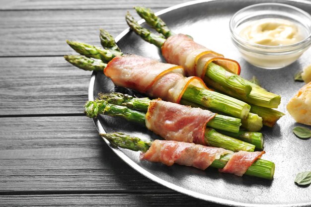 Plate with bacon wrapped asparagus on light background