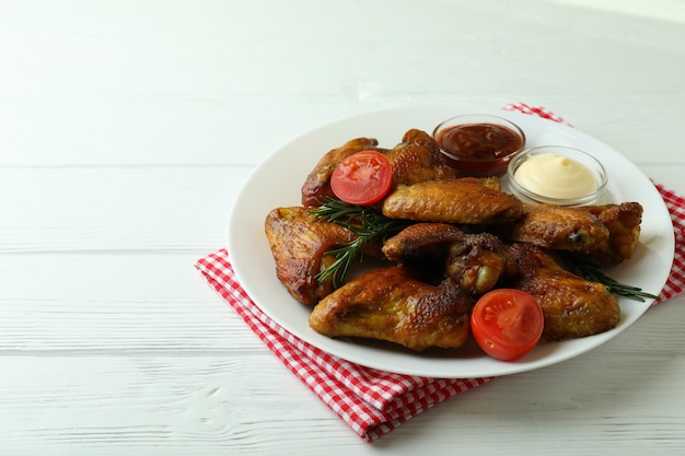 Plate with baked chicken wings and sauces on wooden