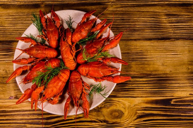 Plate with boiled crayfishes on rustic wooden table. Top view