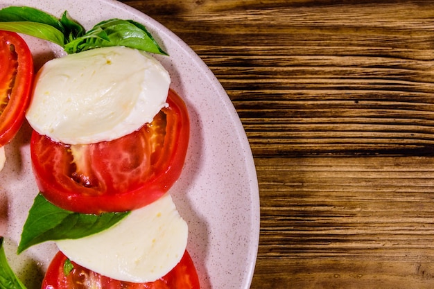 Piatto con insalata caprese insalata italiana con pomodorini mozzarella e foglie di basilico su tavola di legno vista dall'alto