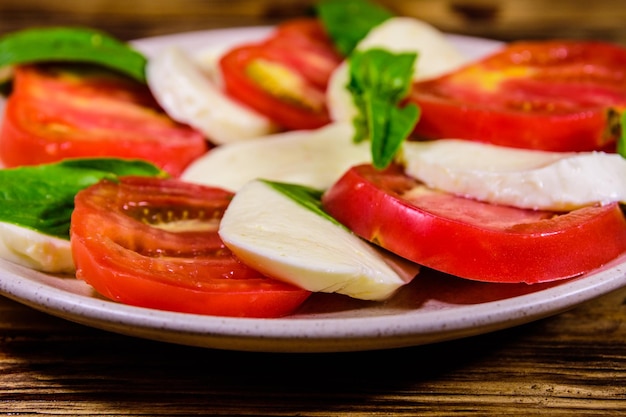 Plate with caprese salad italian salad with cherry tomatoes mozzarella cheese and basil leaves on wooden table