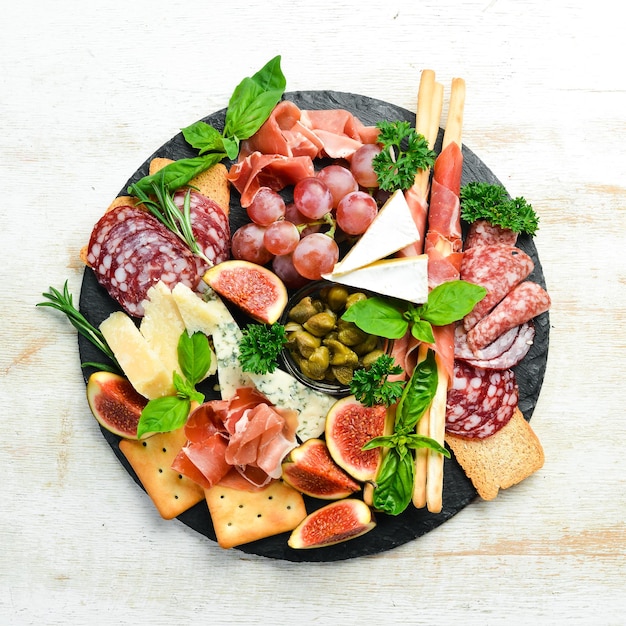 A plate with cheese salami prosciutto and snacks on a black\
stone plate antipasto top view italian food free space for your\
text