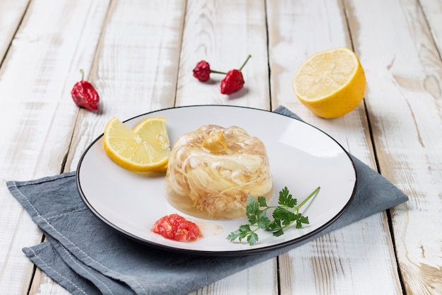 Plate with chicken jelly, decorated with lemon slices, herbs and spices.