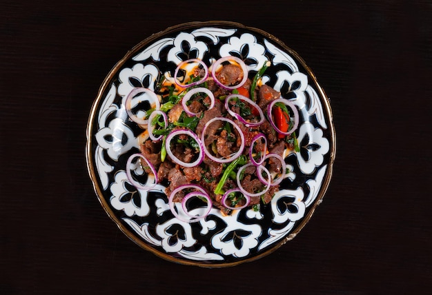 Plate with chopped meat and vegetables on a black background Asian cuisine