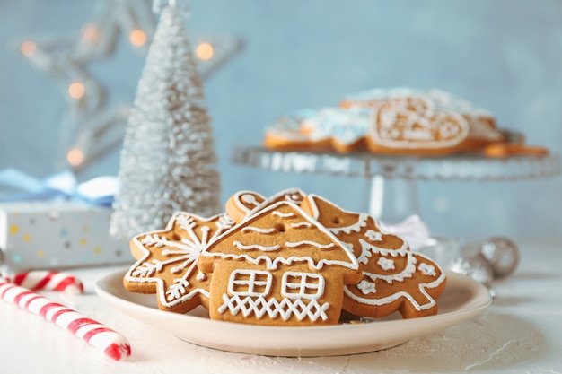 Plate with Christmas cookies, Christmas trees, toys, gift boxes on white table, on blue, closeup