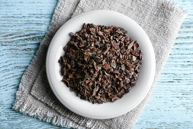 Plate with cocoa nibs on wooden table