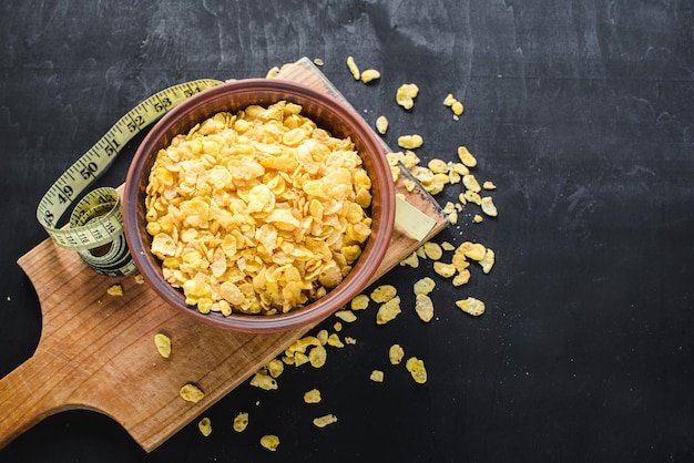 A plate with corn flakes on black wooden background. Healthy food