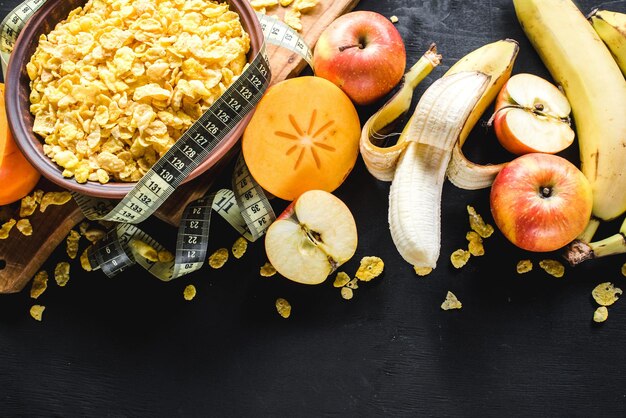 A plate with corn flakes and fruits on black background. Healthy food. Copy space