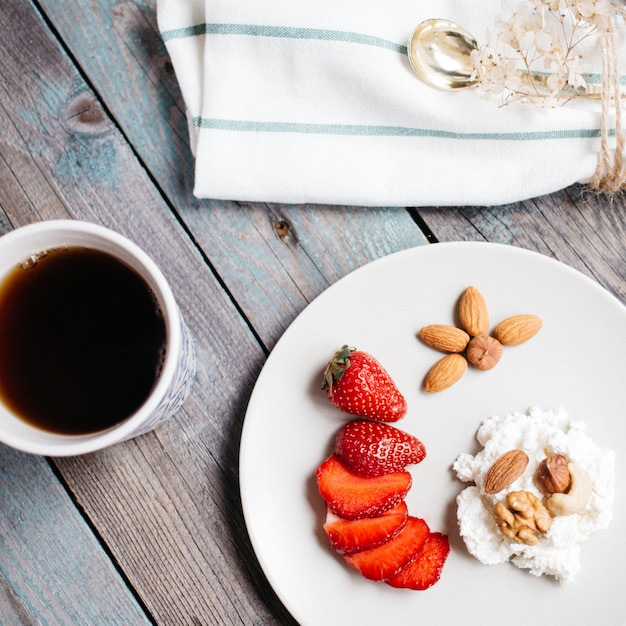 Plate with cottage cheese, strawberries and nuts, a cup of coffee and towels on wooden table, healthy food, breakfast