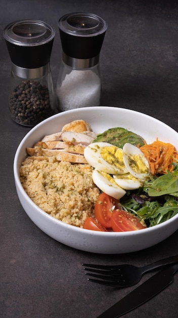 A plate with couscous eggs vegetables and meat on dark background angle view