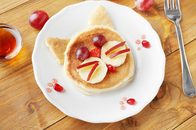 Plate with creative homemade pancake on wooden table