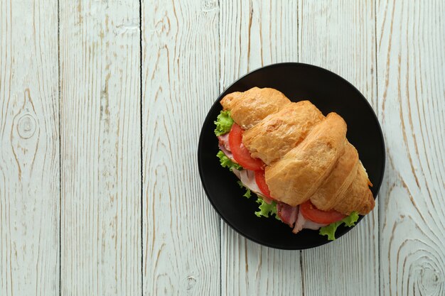 Plate with croissant sandwich on white wooden table