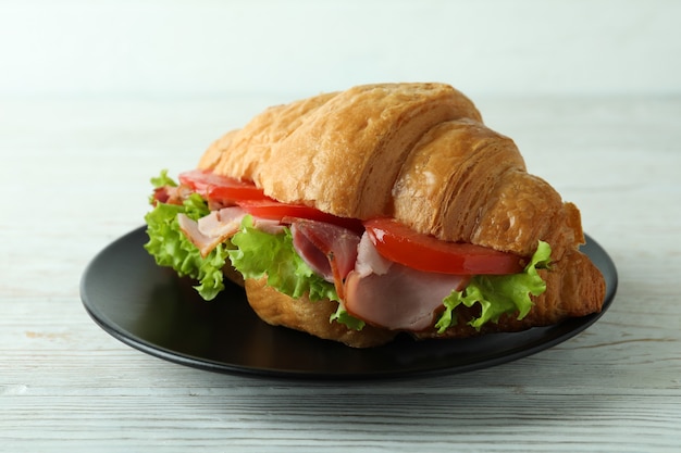 Plate with croissant sandwich on white wooden table