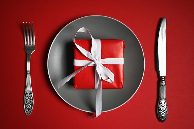 Plate with cutlery and gift on red background. High quality photo