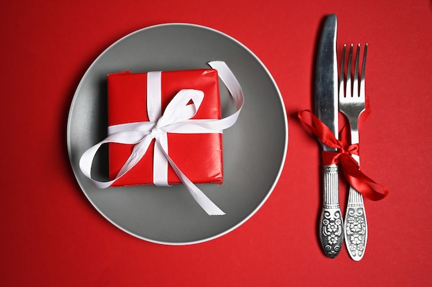 Plate with cutlery and gift on red background. High quality photo