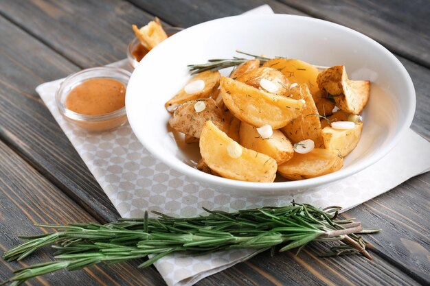 Plate with delicious baked potato wedges and sauce on table