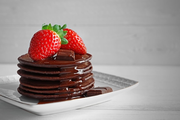 Plate with delicious chocolate pancakes with strawberry on light background