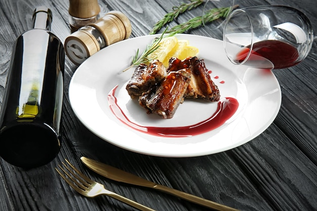 Plate with delicious ribs bottle of wine and glasses on table