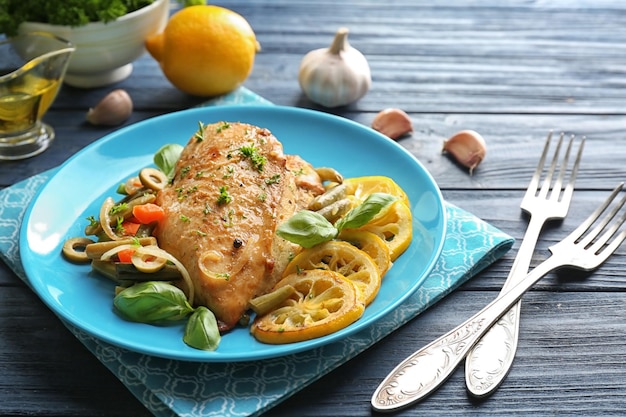 Plate with delicious roasted chicken fillet and sliced lemon on wooden table