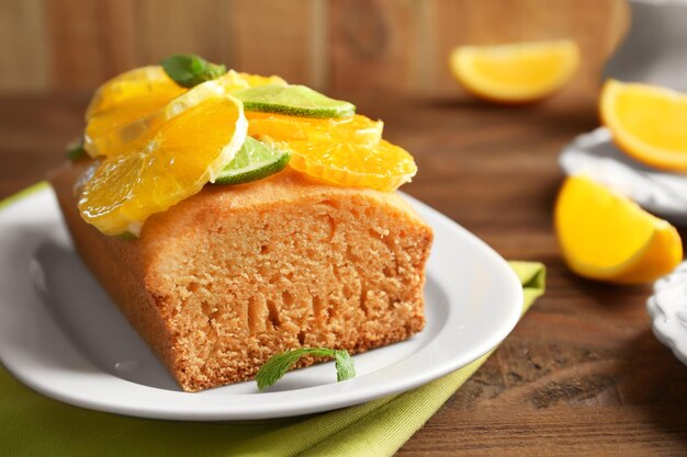 Plate with delicious sliced cake and citrus fruit on wooden table