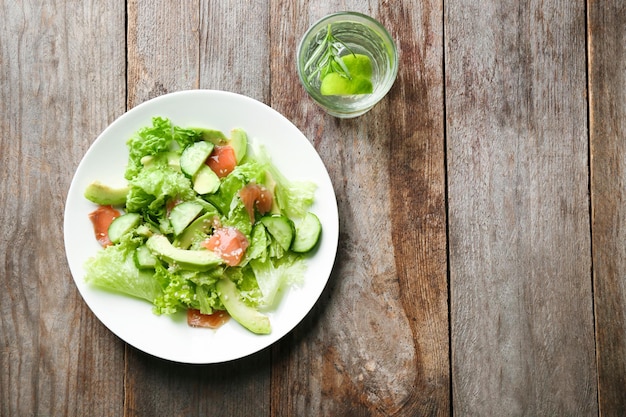 Plate with delicious vegetable salad on wooden background top view
