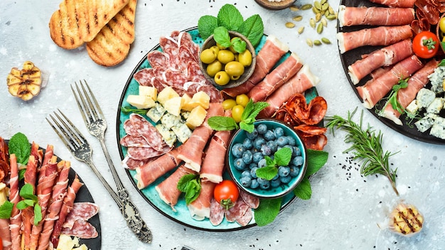Plate with different kinds of cheese and ham prosciutto jamon salami and snacks Antipasto Dinner or aperitif party concept On a gray stone background