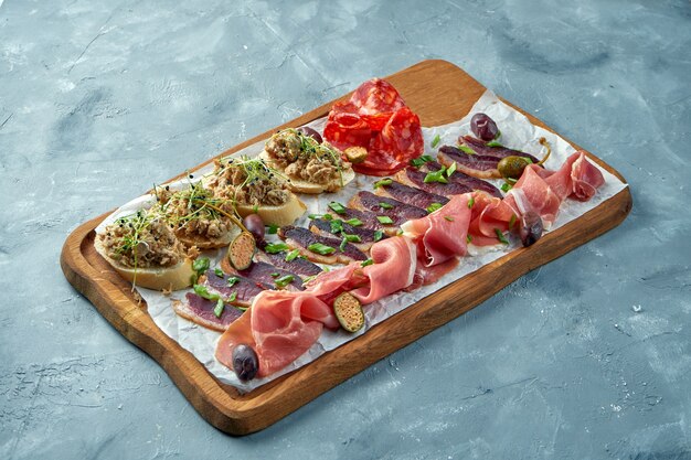 Plate with different types of meat antipasto - sliced prosciutto, chorizo, jerky duck and Bruschetta with stew on a wooden board