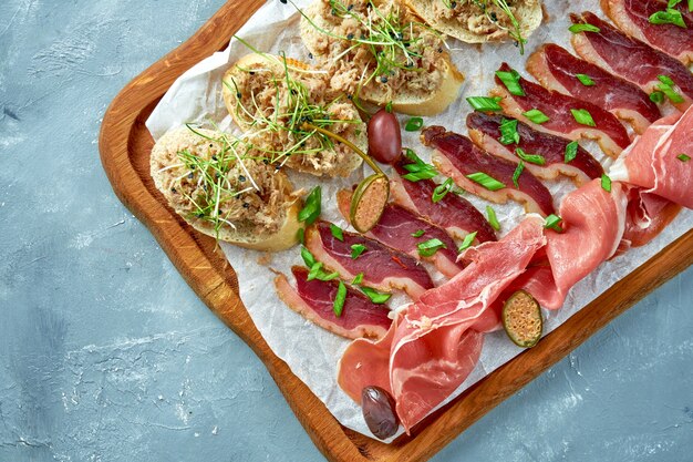 Plate with different types of meat antipasto - sliced prosciutto, chorizo, jerky duck and bruschetta with stew on a wooden board