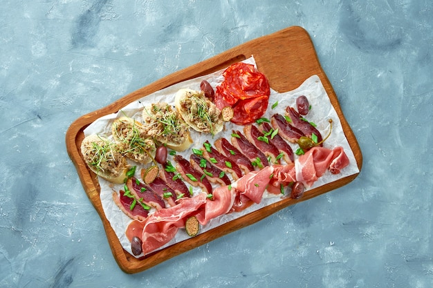 Plate with different types of meat antipasto - sliced prosciutto, chorizo, jerky duck and Bruschetta with stew on a wooden board.