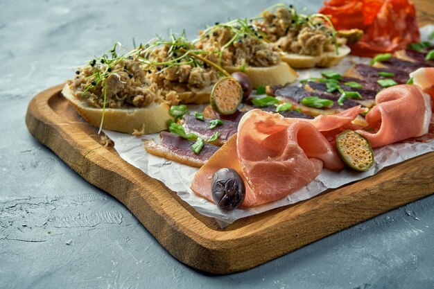 Plate with different types of meat antipasto - sliced prosciutto, chorizo, jerky duck and Bruschetta with stew on a wooden board.