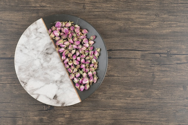 Un piatto con fiori di rosa appassiti su un legno.