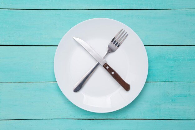 Plate with fork and knife on blue wooden background Top view