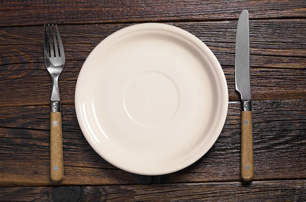 Plate with fork and knife on dark wooden table, top view