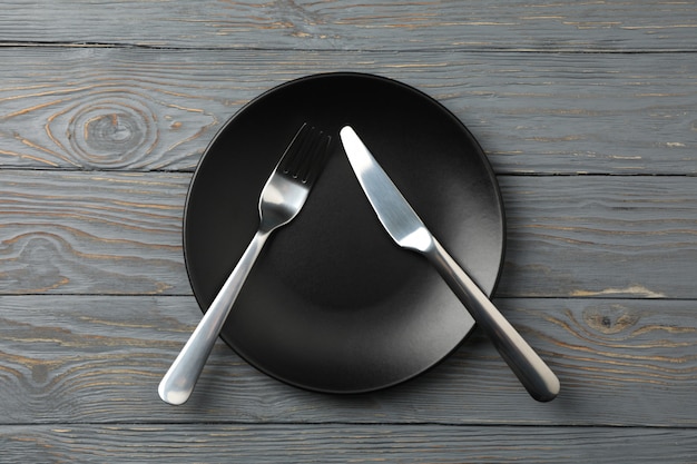 Plate with fork and knife on wooden background, top view