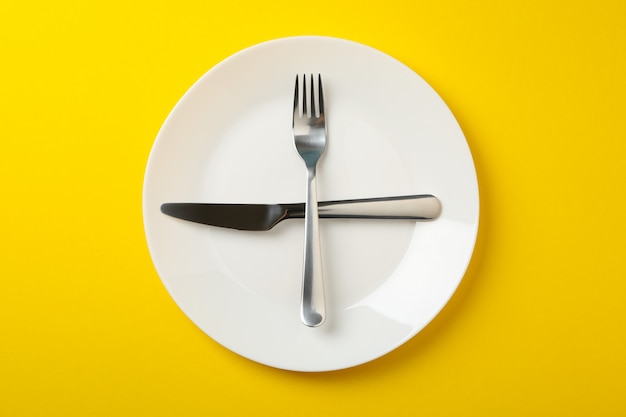 Plate with fork and knife on yellow background, top view