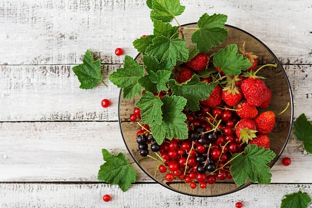 Plate with fresh berries (strawberries and currants) on dark wooden background