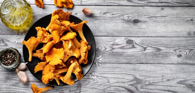 Photo a plate with fresh chanterelles mushrooms on gray rustic wooden background top view long banner copy space