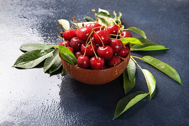 Foto piastra con ciliegie fresche con foglie verdi. sfondo nero.