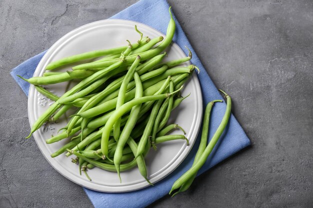 Plate with fresh green beans on grey background