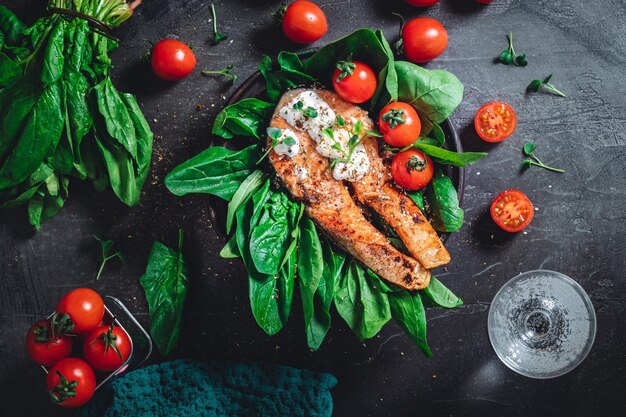 Foto un piatto con spinaci crudi verdi freschi e pomodorini fritti di salmone selvatico e salsa di crema di formaggio