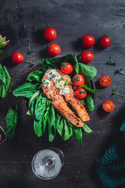 Un piatto con spinaci crudi verdi freschi e pomodorini fritti di salmone selvatico e salsa di crema di formaggio