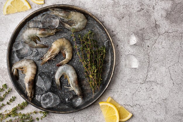 Plate with fresh shrimps raw prawns with lemon slices ice cubes and thyme on a gray background