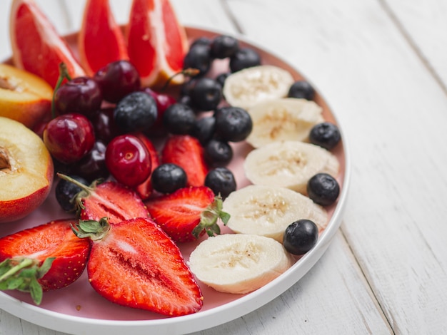 Plate with fresh summer fruits. Strawberry, blueberry, sweet cherry on wood white