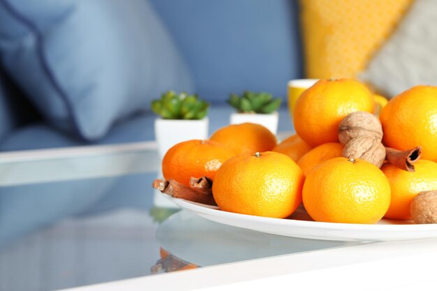 Plate with fresh tangerines on table in living room, close up